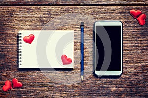 Empty notebook, pencil and red heart on wood table with phone bl