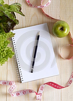 Empty notebook with vegetable salad and apple