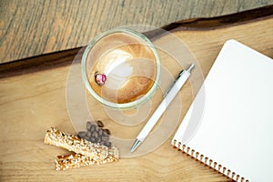 Empty notebook, white pen and cappuccino coffee on wooden table, top view