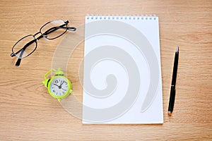 Empty notepad with alarm clock, pen and eyeglasses on table
