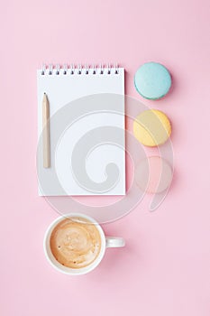 Empty notepad, coffee and colorful macaron on pink pastel desk top view. Cozy morning breakfast. Fashion flat lay.