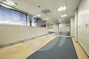 An empty office with two-tone carpeted floors, a space with partitions and filing cabinets throughout and technical ceilings and