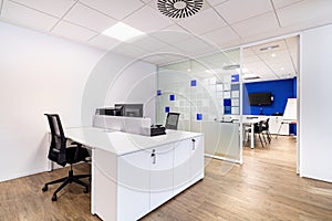 Empty office with work spaces. Modern office interior with blue and white walls. Meeting room at the background.