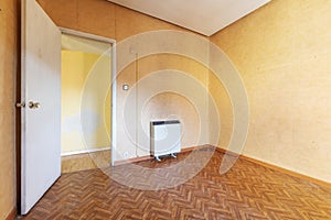 Empty and old room with wood-like sintasol floors, electric heat accumulator radiator and papered walls