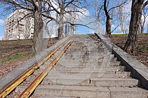 Empty old stairs with rusted metal rails without any people, which going up to the blue sky, surrounded by dry trees and