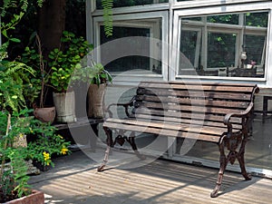 Empty old wooden bench on terrace in front of the old white glass house near the green houseplant and garden