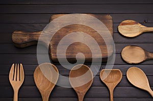 An empty old wooden cutting board with a spoon and fork arranged on an old black wooden table - top view
