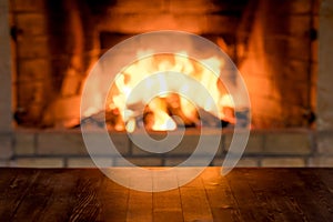 Empty old wooden table against burning wood in the fireplace