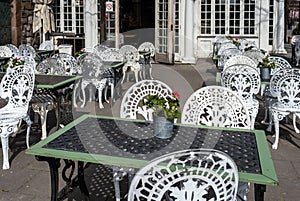 Empty outdoor cozy cafe with beautiful white chairs and wooden tables decorated with red flowers geranium. Restaurant on the