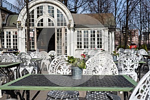 Empty outdoor cozy cafe with beautiful white chairs and wooden tables decorated with red flowers geranium. Restaurant on the