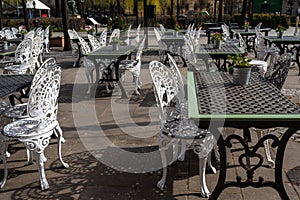 Empty outdoor cozy cafe with beautiful white chairs and wooden tables decorated with red flowers geranium. Restaurant on the