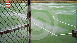 Empty outdoor green basketball court with visible cracks and white lines view thru open gate