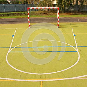 Empty outdoor handball playground, plastic light green surface on ground. Empty gate.