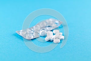 Empty pack with white pills packed in blister with copy space on blue background. Focus on foreground, soft bokeh