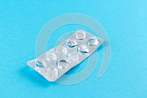 Empty pack of white pills packed in blister with copy space on blue background. Focus on foreground, soft bokeh