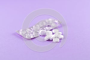 Empty pack with white pills packed in blister with copy space on purple background. Focus on foreground, soft bokeh