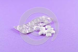Empty pack with white pills packed in blister with copy space on purple background. Focus on foreground, soft bokeh