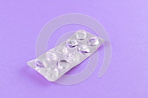 Empty pack of white pills packed in blister with copy space on purple background. Focus on foreground, soft bokeh