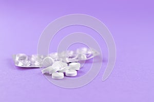 Empty pack with white pills packed in blister with copy space on purple background. Focus on foreground, soft bokeh