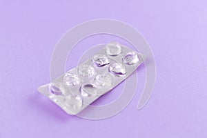 Empty pack of white pills packed in blister with copy space on purple background. Focus on foreground, soft bokeh