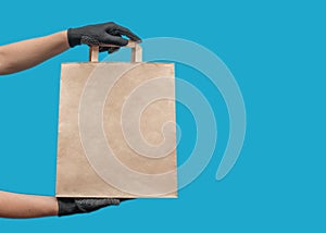 Empty paper bag. Shopping bag for groceries. Hands in black gloves. On a blue background