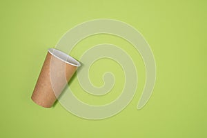 An empty paper cup for coffee lies on a green background