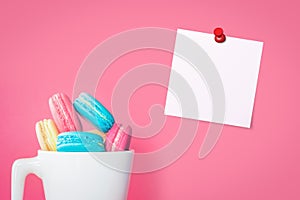 Empty paper note sheet with push pins with macaroons on pink background