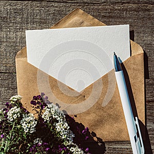 An empty paper postcard, an envelope and alissum flowers on a wooden background, a postcard layout with a place to copy