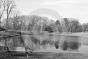 Empty park bench facing windmill and pond