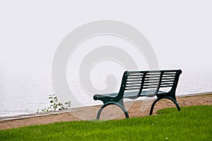 Empty park bench, wet from the rain on the shore of a misty lake