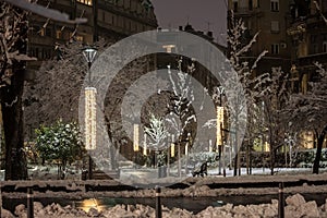 Empty park covered in snow in Serbia, in Eastern Europe, In Belgrade, Serbia, with public lamps and trees during a freezing dark