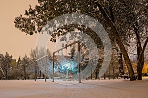 Empty park swings during a Winter night, after a few snow heavy hours. Quiet outdoor place in Bucharest, Romania