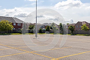 Empty parking lot with lined spaces - lone light pole - suburban homes background - clear sky with clouds