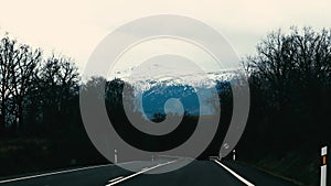 An empty paved straight road to mountain with snow-capped peaks in winter. A journey through mountains in wintertime