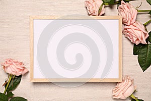 Empty photo frame and beautiful rose flowers on wooden background, flat lay. Mockup for design