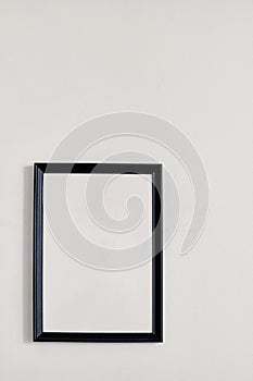 An empty photo frame with a black border hanging on a white wall