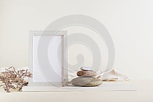 Empty photo frame, dried flowers and stones on a light background