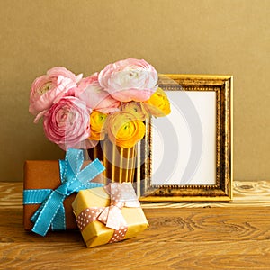 Empty photo frame with gift boxes and flowers on wooden table