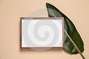 Empty photo frame and green leaf on beige background, flat lay. Space for design