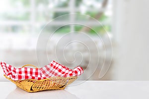 Empty picnic basket. Close-up of a empty straw basket with a checkered red napkin on table over blurred kitchen background. For