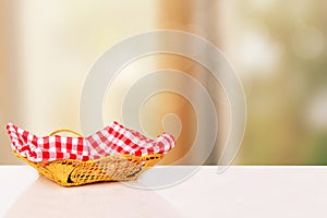 Empty picnic basket. Close-up of a empty straw basket with a checkered red napkin on table over blurred kitchen background. For