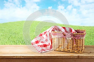 Empty picnic basket and tablecloth on wooden table over landscape background. Shavuot holiday mock up for design