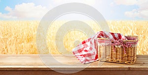 Empty picnic basket and tablecloth on wooden table over wheat field landscape background. Shavuot holiday mock up for design and