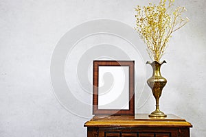 empty picture frame mockup and gypsophila flowers vase on wooden table near grunge wall, autumn fall concept.
