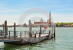 An empty pier overlooks the city canal against the background of the old city on the other side of the canal and the blue sky