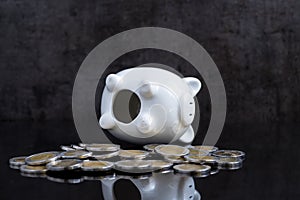 Empty piggy bank lay on dark black table with coins using as bro