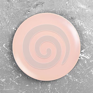 Empty pink or coral round plate on grey cement table background. Top view, template for your design