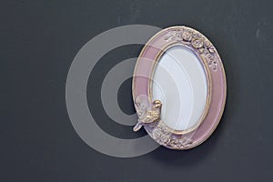 Empty pink-gold vintage oval frame in Victorian style on a gray wall, background or concept