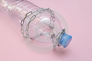 Empty plastic bottle in chains on a pink background. Water scarcity and drought concept. Great value of water. Help.