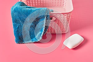 Empty plastic square basket for washing with blue soft towel near antibacterial soap lies on pink countertop in laundry